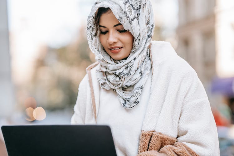 Positive Arab Female Freelancer Typing On Netbook In City