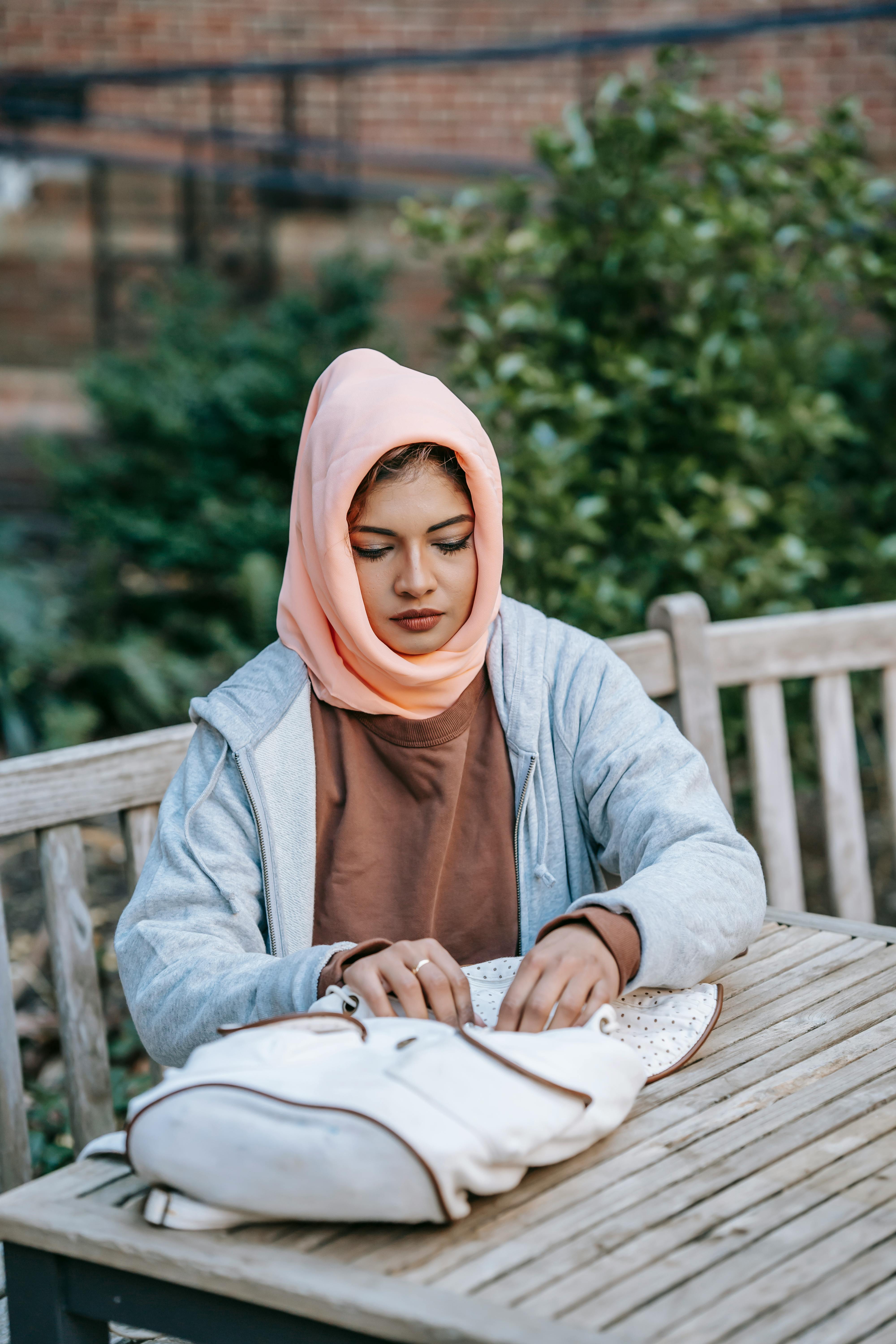 thoughtful young arab lady with backpack sitting at table in park