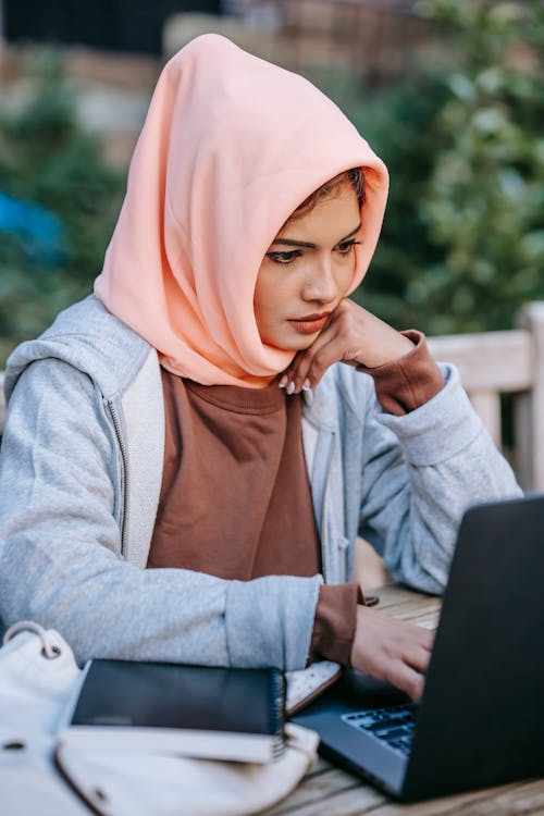 Serious young ethnic female freelancer browsing laptop in cafe