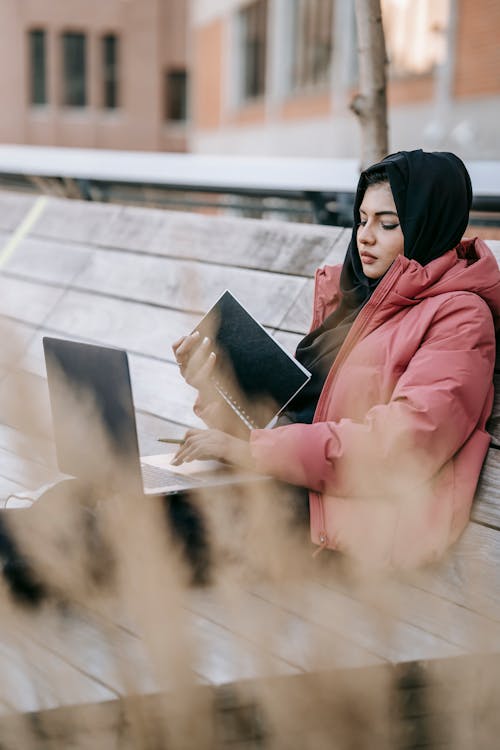 Young freelancer surfing internet on laptop sitting on bench on street