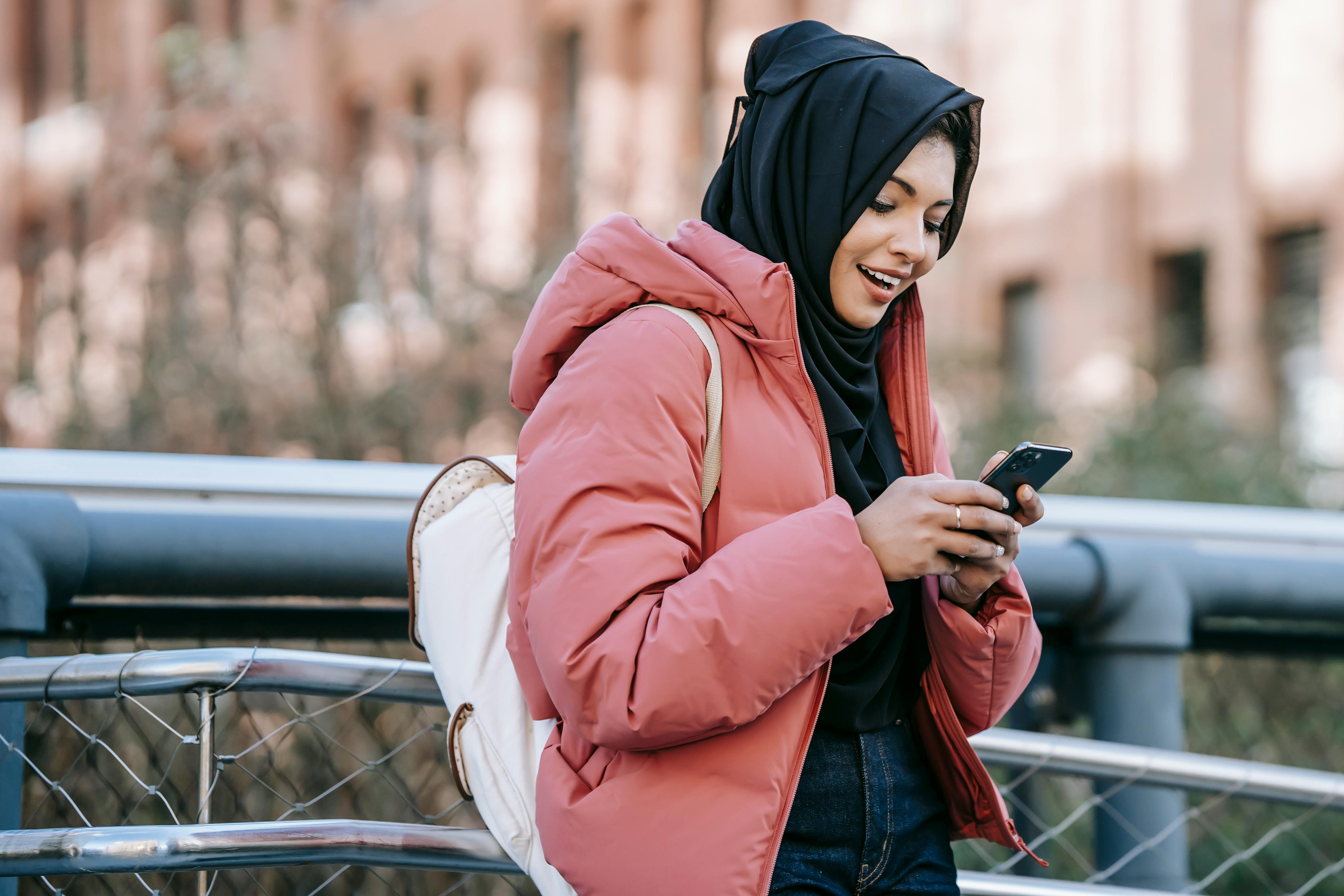 muslim smiling ethnic woman in hijab checking smartphone