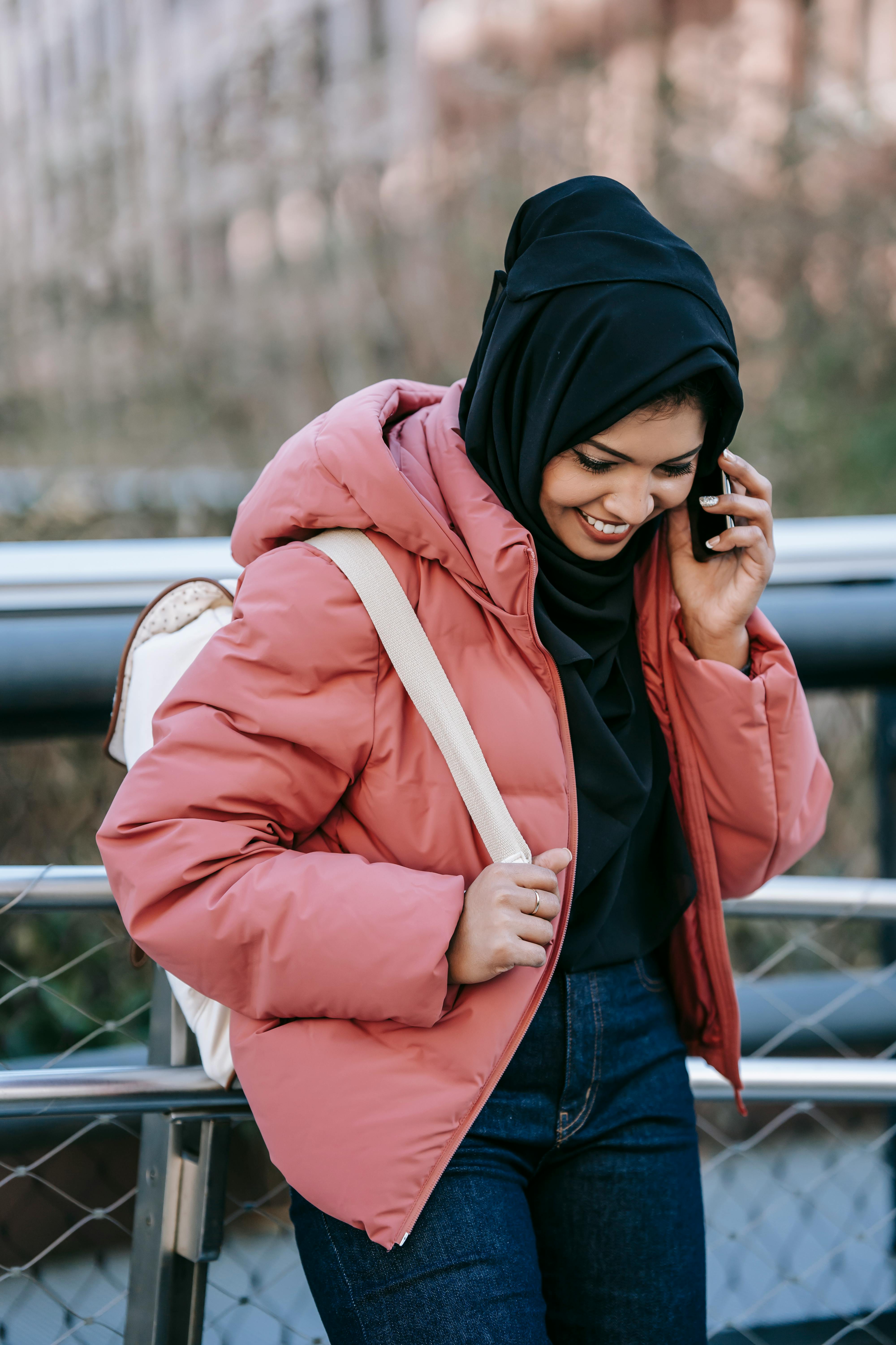 cheerful muslim woman speaking on smartphone on street in daytime