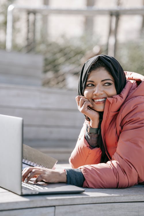 Free Positive Muslim female freelancer browsing laptop on street Stock Photo