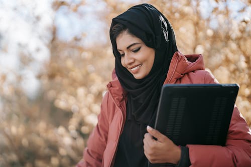검은 Hijab와 검은 색 노트북 컴퓨터를 들고 갈색 코트에 여자