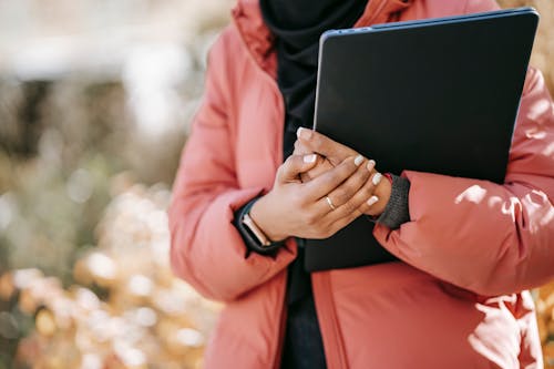 Pessoa De Jaqueta Rosa Segurando Um Laptop Preto