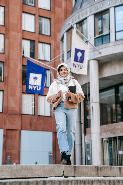 Positive Muslim female student standing on street against buildings of university