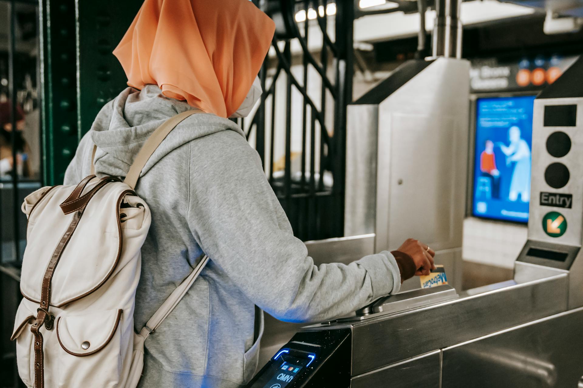 Back view Muslim woman in casual outfit and hijab with backpack using travel card for passing metro gate at daytime