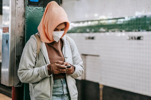Unrecognizable ethnic lady standing in mask in subway with cellphone