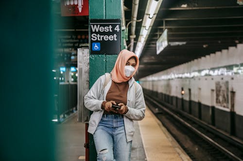 Faceless ethnic female standing in metro in mask with smartphone