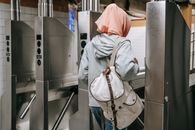 Back view of unrecognizable Muslim woman in casual clothes with backpack and hijab walking through turnstile in metro