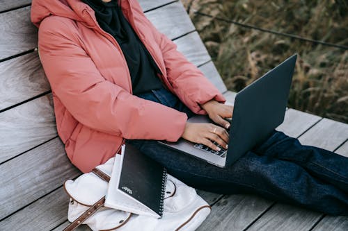 Free Side view of unrecognizable woman in casual outfit browsing laptop sitting on bench in park Stock Photo