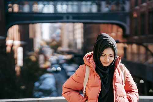 Free Ethnic young lady in warm clothes and hijab standing on bridge in street near buildings in daytime Stock Photo