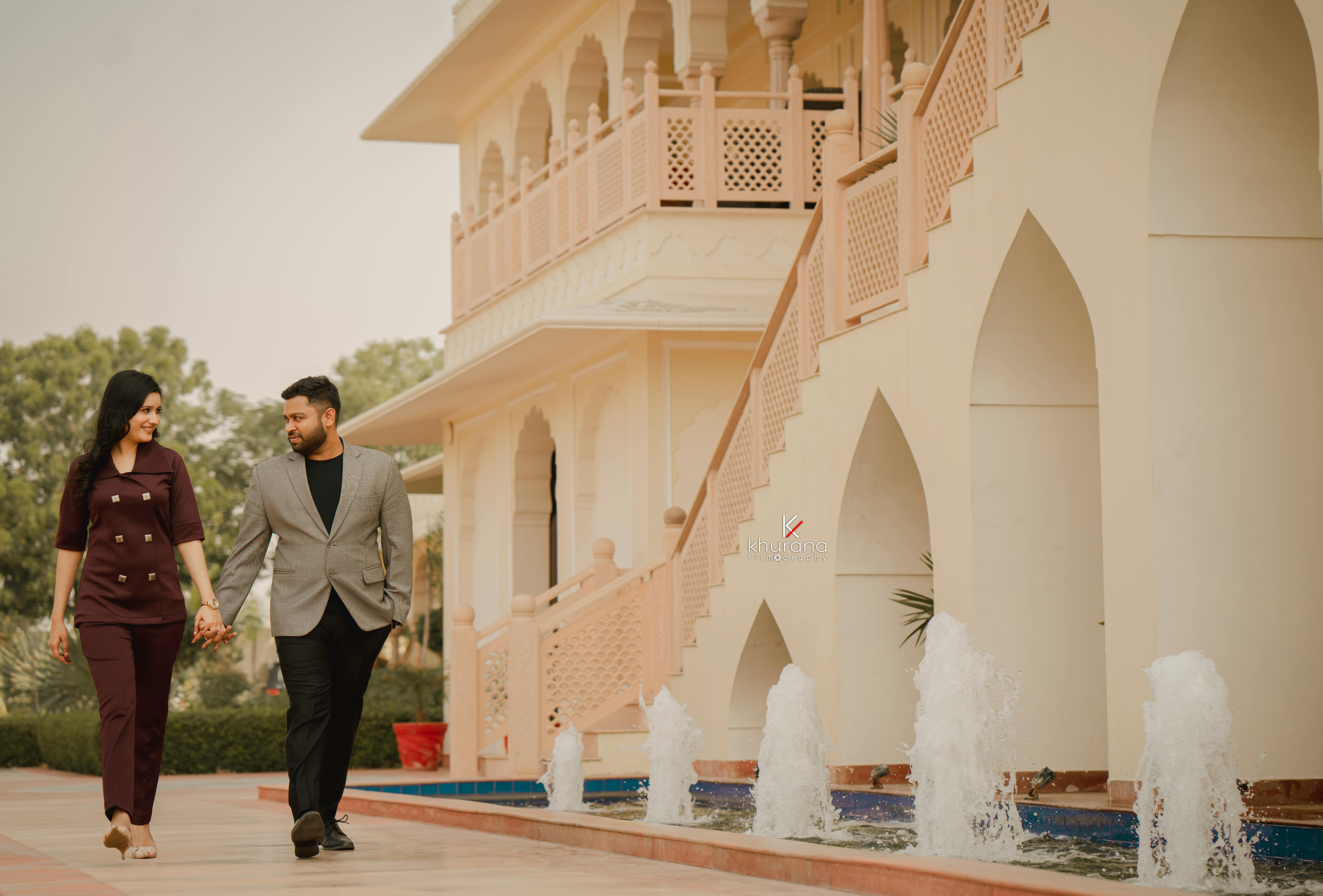 A couple holding hands and smiling outdoors near a fountain in Jaipur, India.