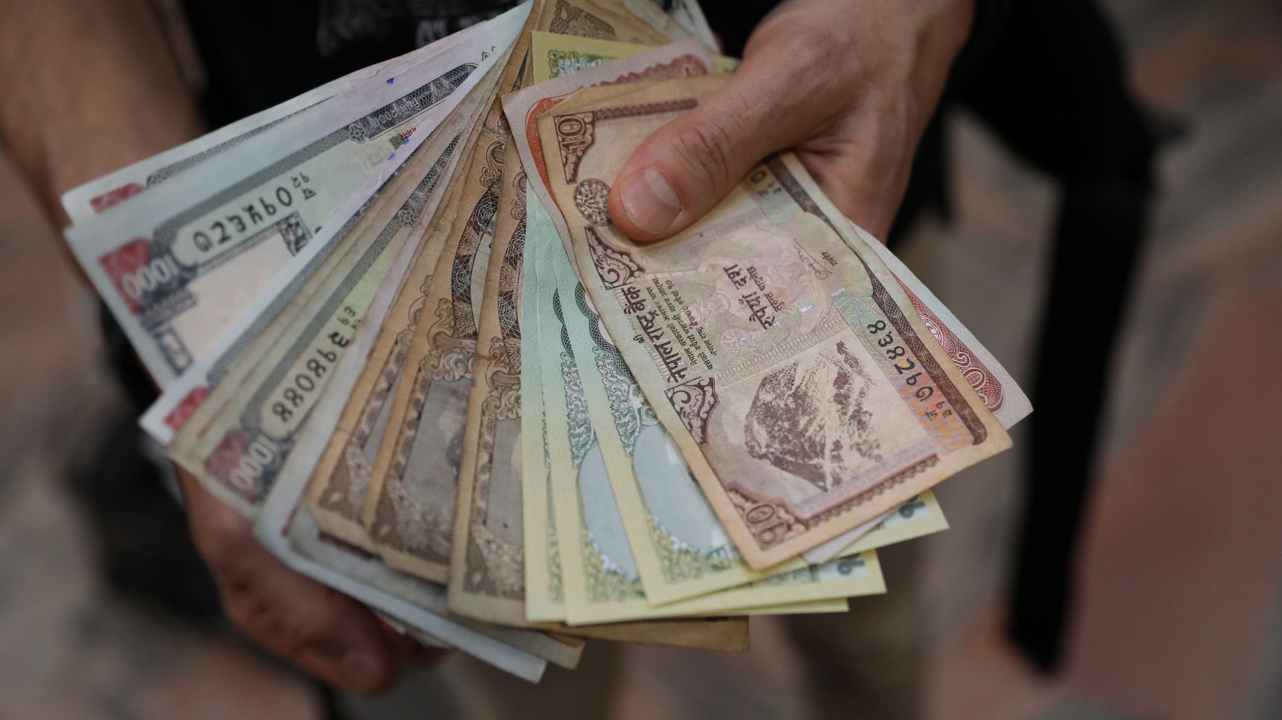 A close-up of hands holding a fan of Nepalese rupee banknotes showcasing various denominations.