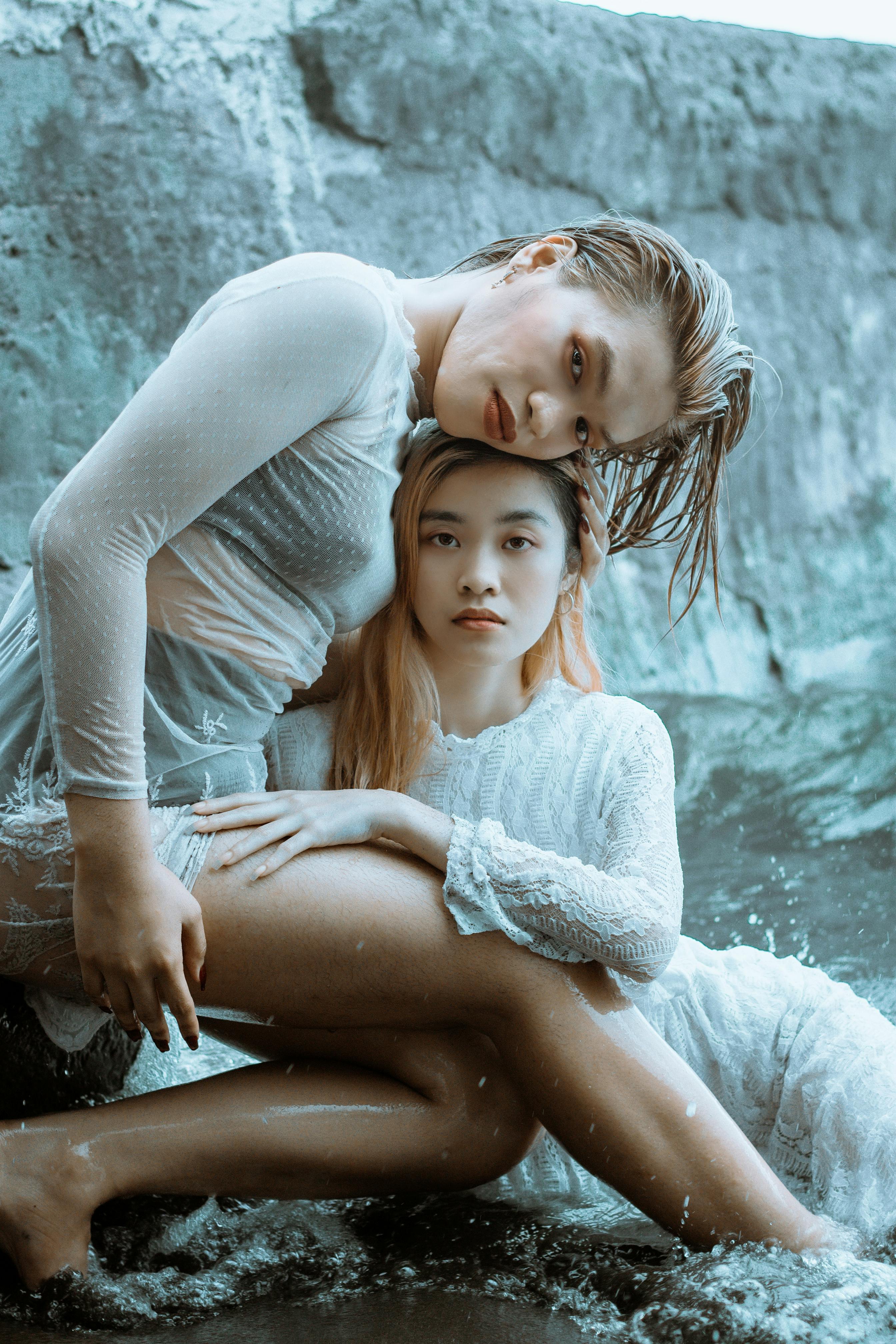 young woman sitting on stone and hugging girlfriend