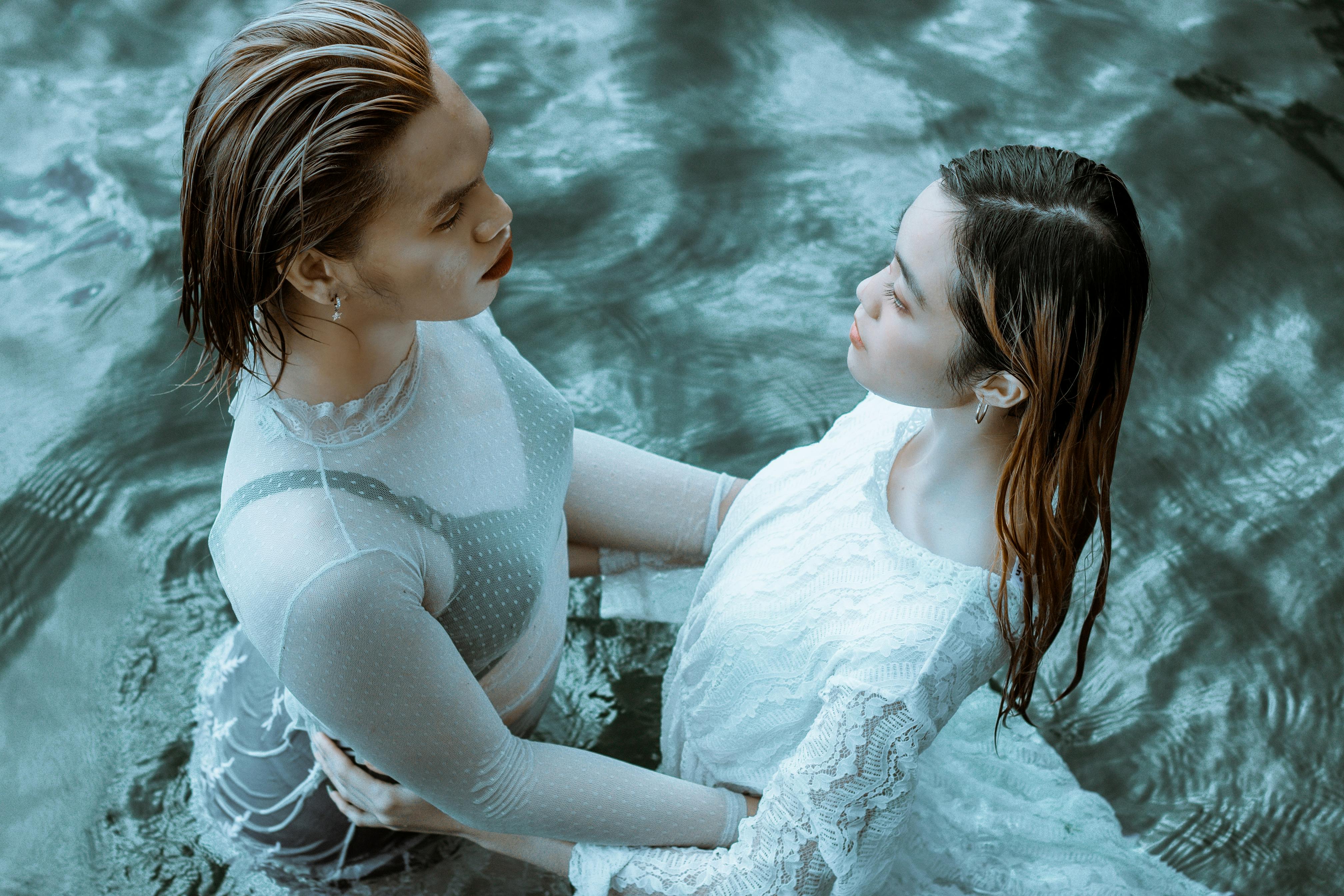 serene young girlfriends hugging in clear blue water