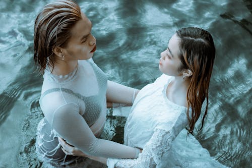 Serene young girlfriends hugging in clear blue water