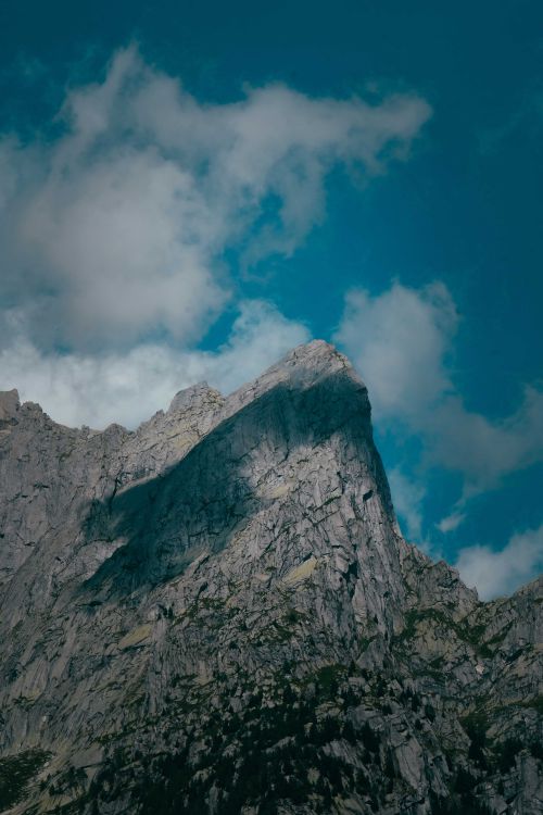 Free Tall rocky steep cliff with rough surface and sharp peak located in nature with shadow of clouds in sunny weather Stock Photo