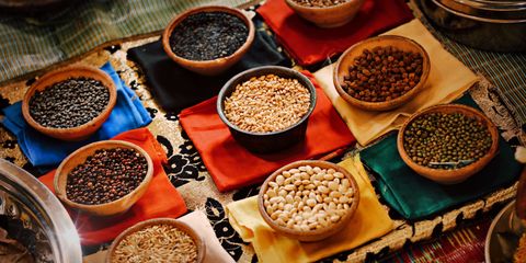 A vibrant assortment of grains and beans in ceramic bowls arranged on colorful textiles, showcasing diverse ingredients.