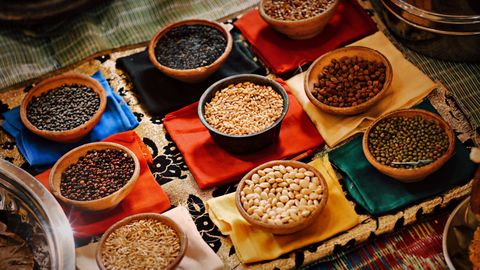 A vibrant assortment of grains and beans in ceramic bowls arranged on colorful textiles, showcasing diverse ingredients.