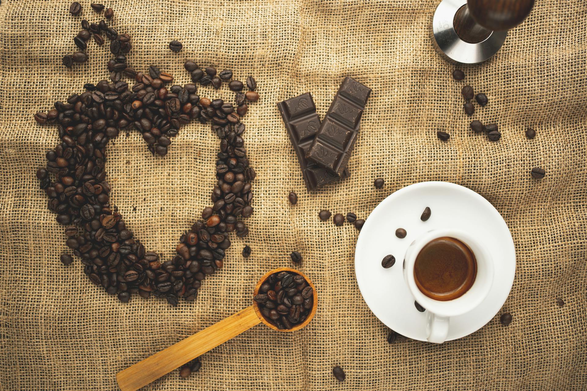 Flat lay of coffee beans, chocolate, and espresso on burlap for a rustic coffee theme.