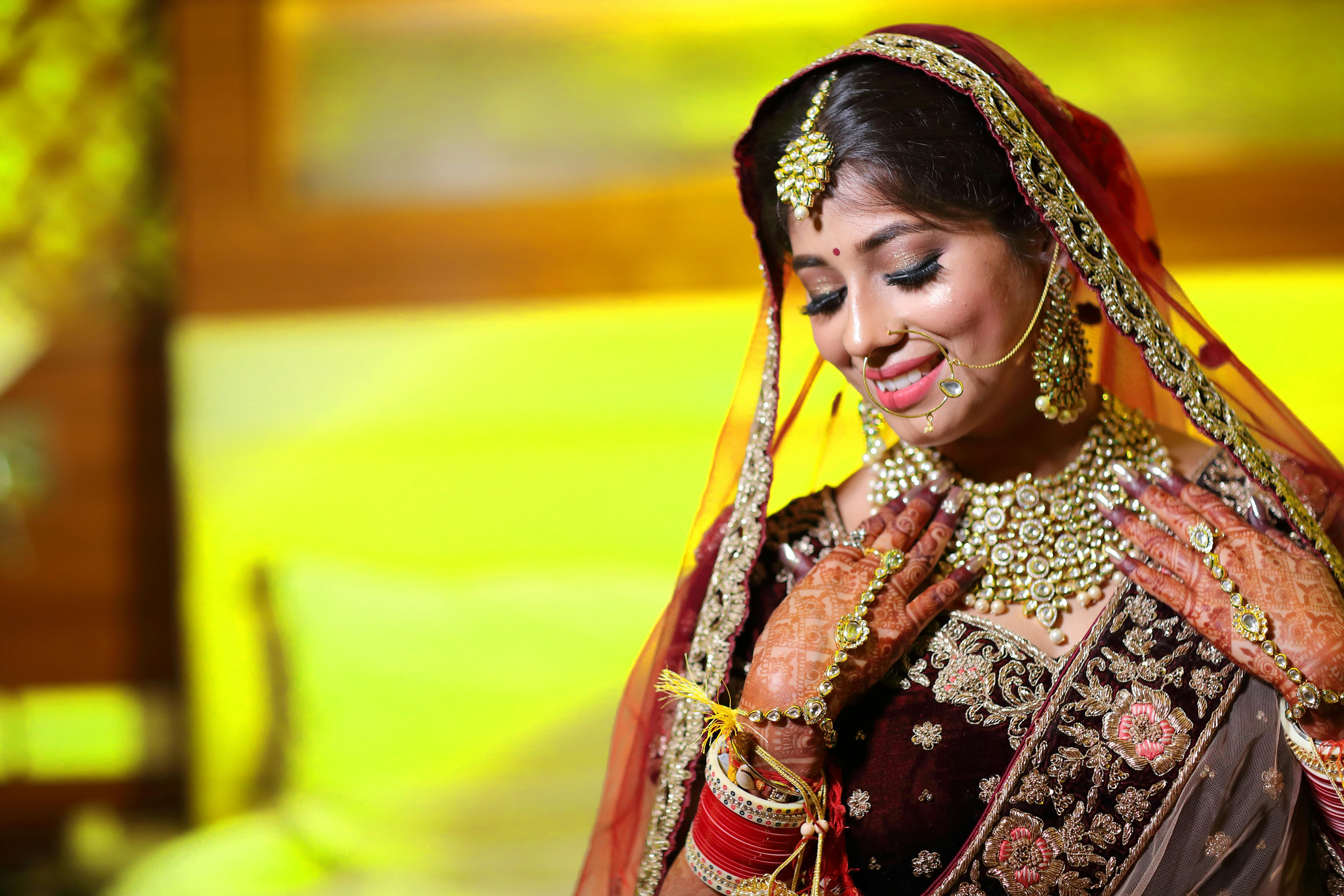 Beautiful Indian bride smiling in traditional wedding attire with intricate jeweleries and henna in Delhi, India.