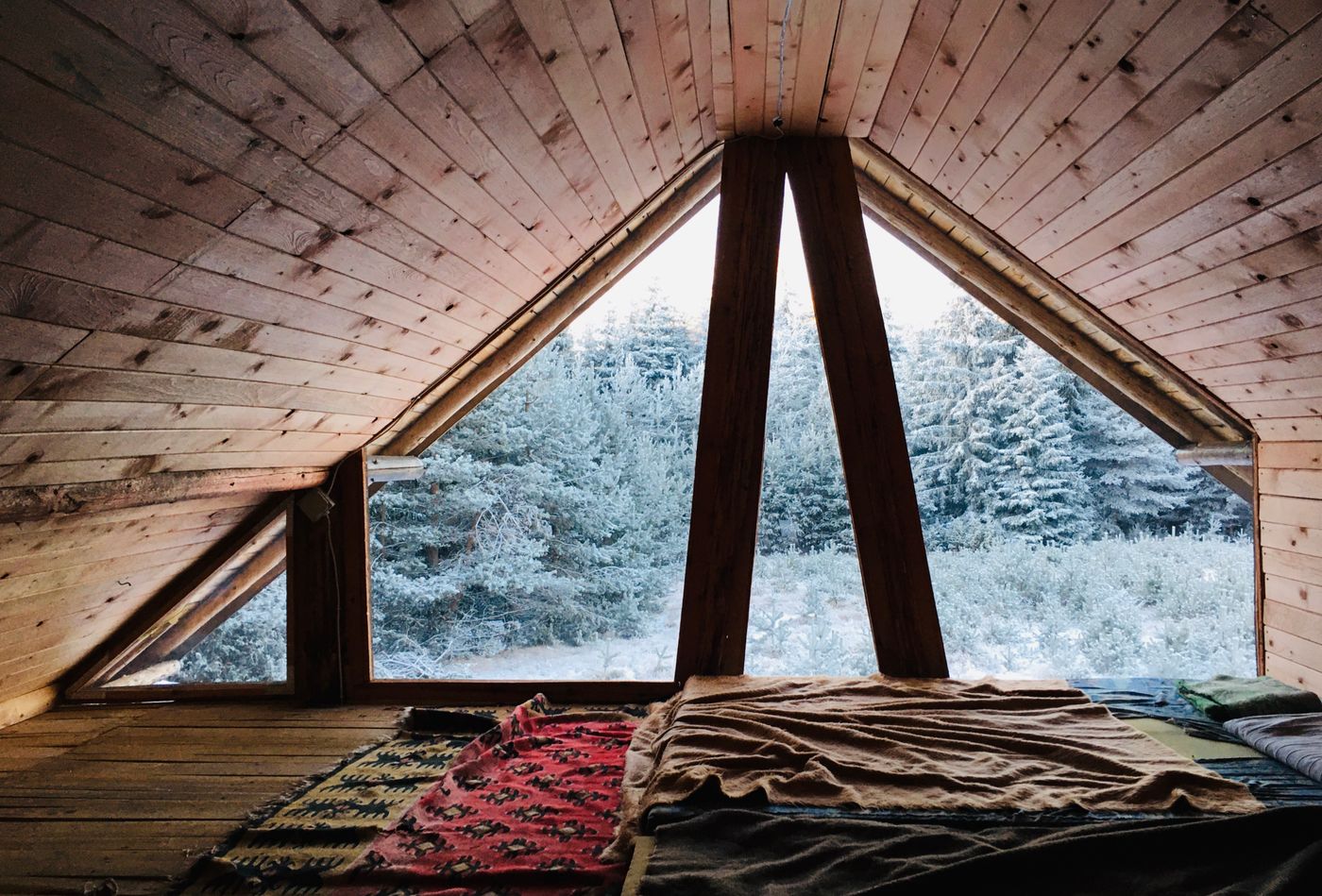 A warm wooden cabin nook with blankets, overlooking a snowy forest