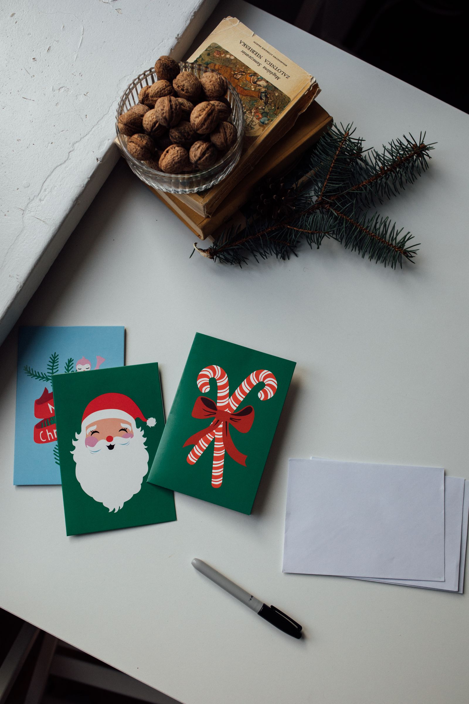 Christmas cards, envelopes, a pen, and seasonal decorations arranged on a table.