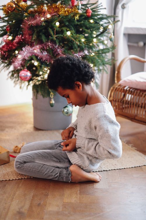 Free A child sitting by a decorated Christmas tree, enjoying the festive atmosphere. Stock Photo