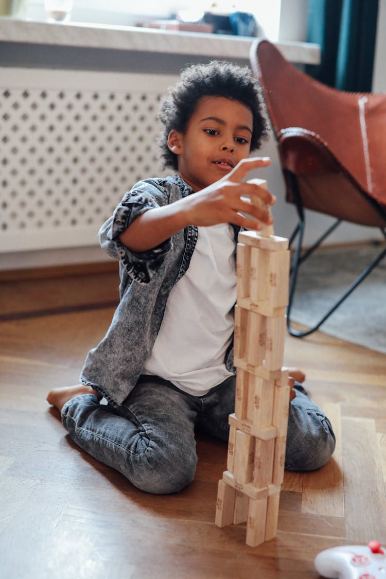 Boy Sitting On Parquet Floor Building Tower With Jenga Blocks