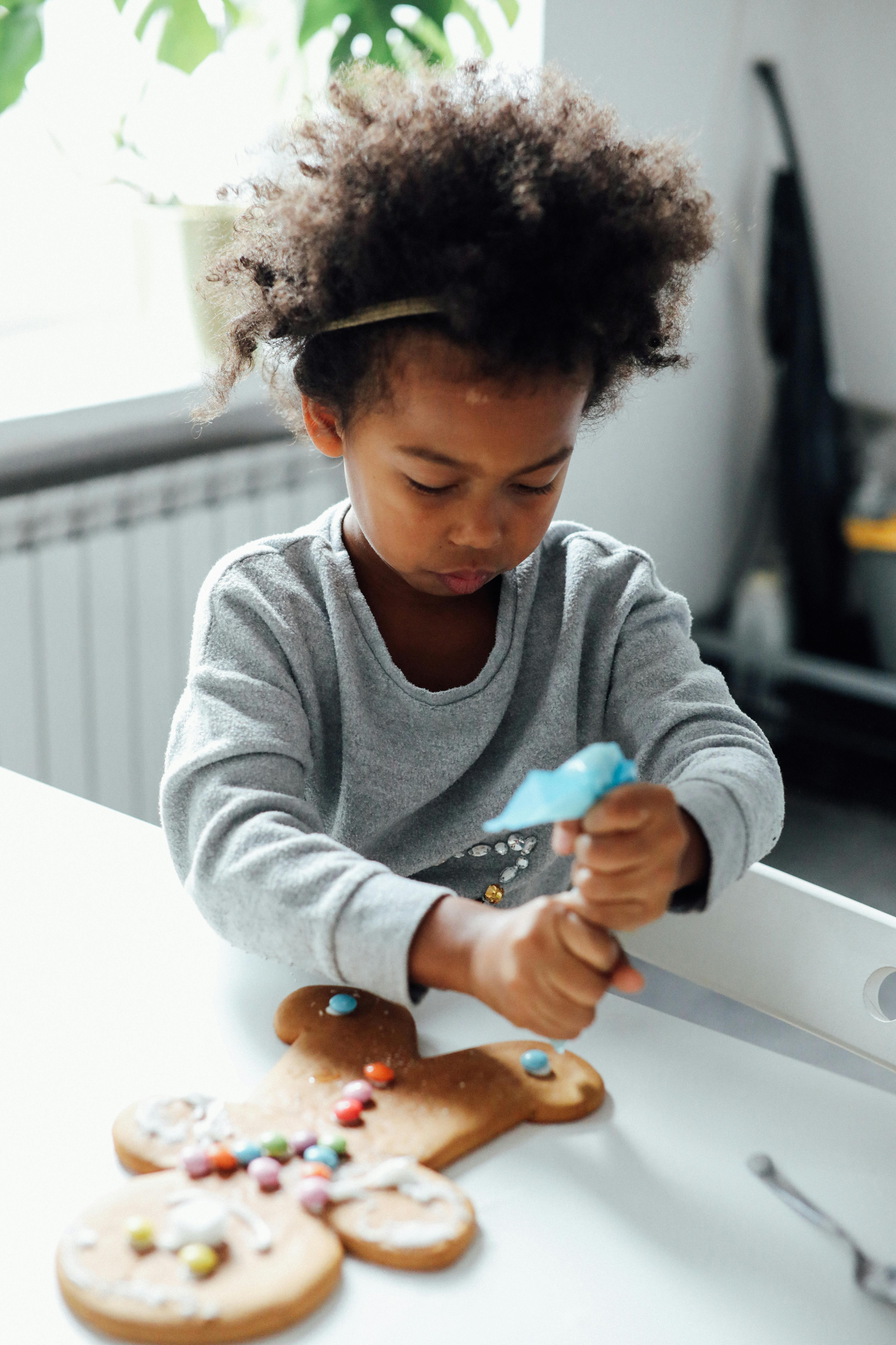 A young child joyfully decorates a gingerbread man indoors for the festive Christmas season.