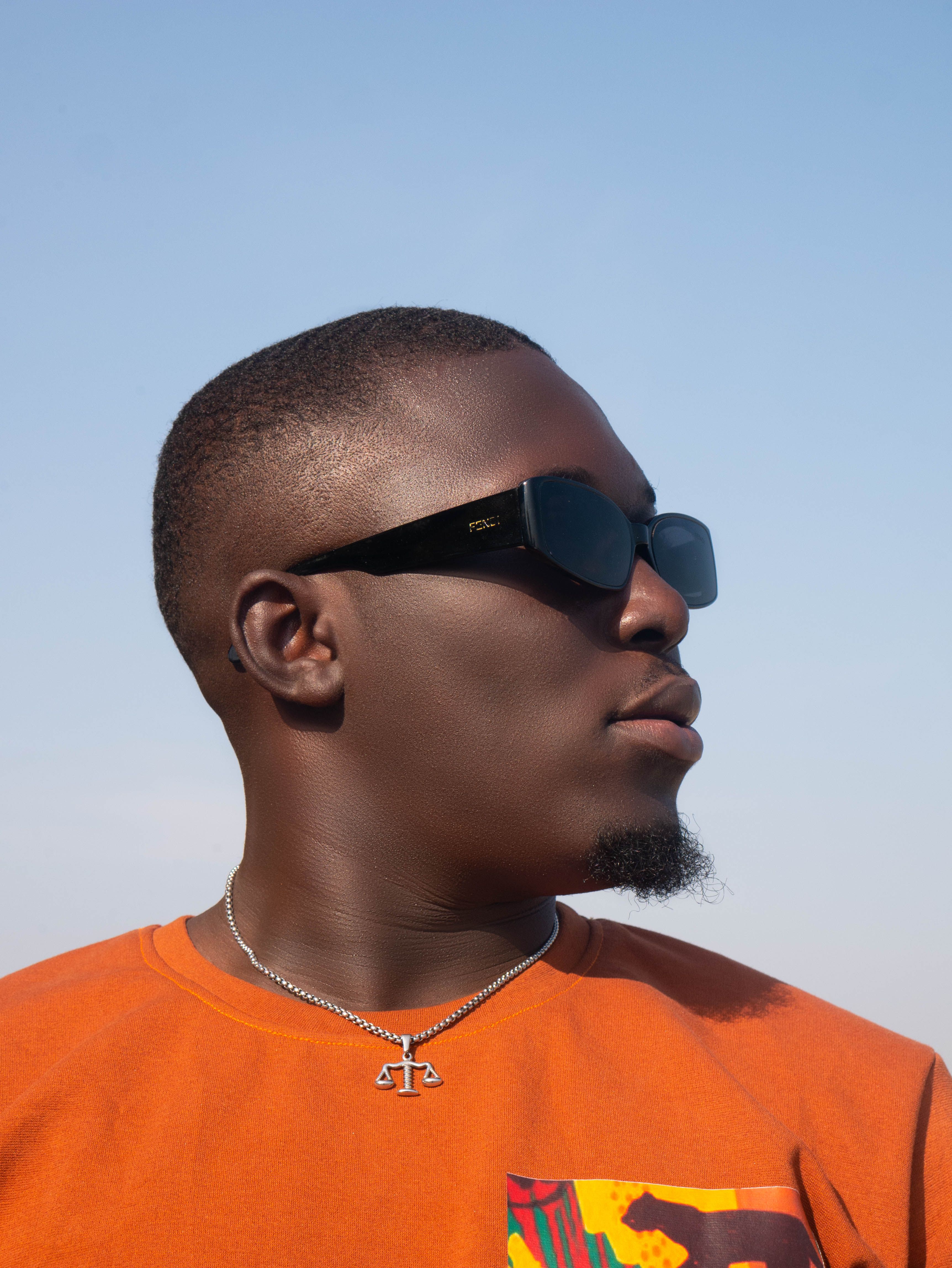 Portrait of a fashionable man wearing sunglasses and an orange shirt against a clear blue sky.