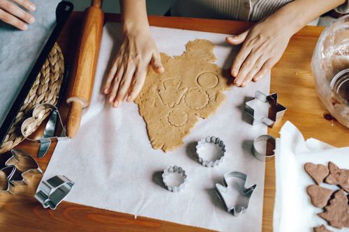 Free Hands rolling and cutting dough for homemade cookies with baking tools on a wooden table. Stock Photo