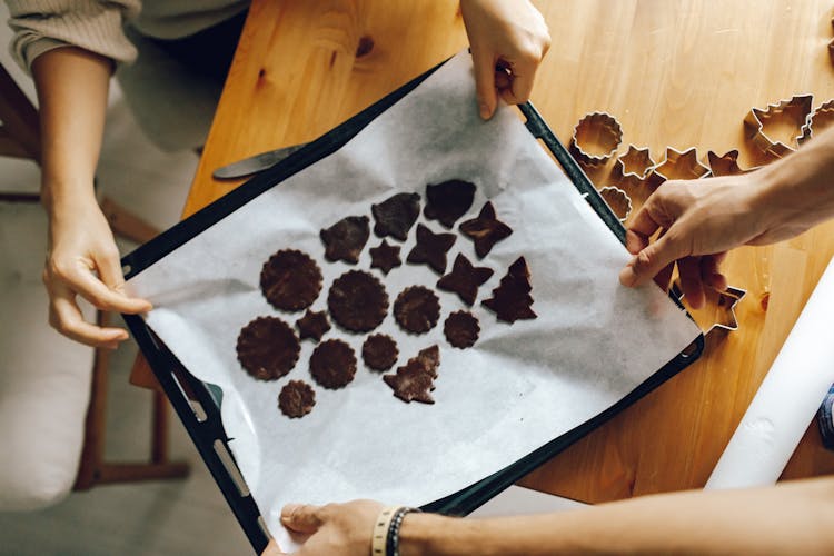 Hands Holding White Wax Paper With Brown Dough In Various Shapes