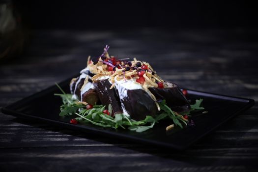 Close-up of a stylishly plated eggplant salad with arugula and pomegranate seeds.