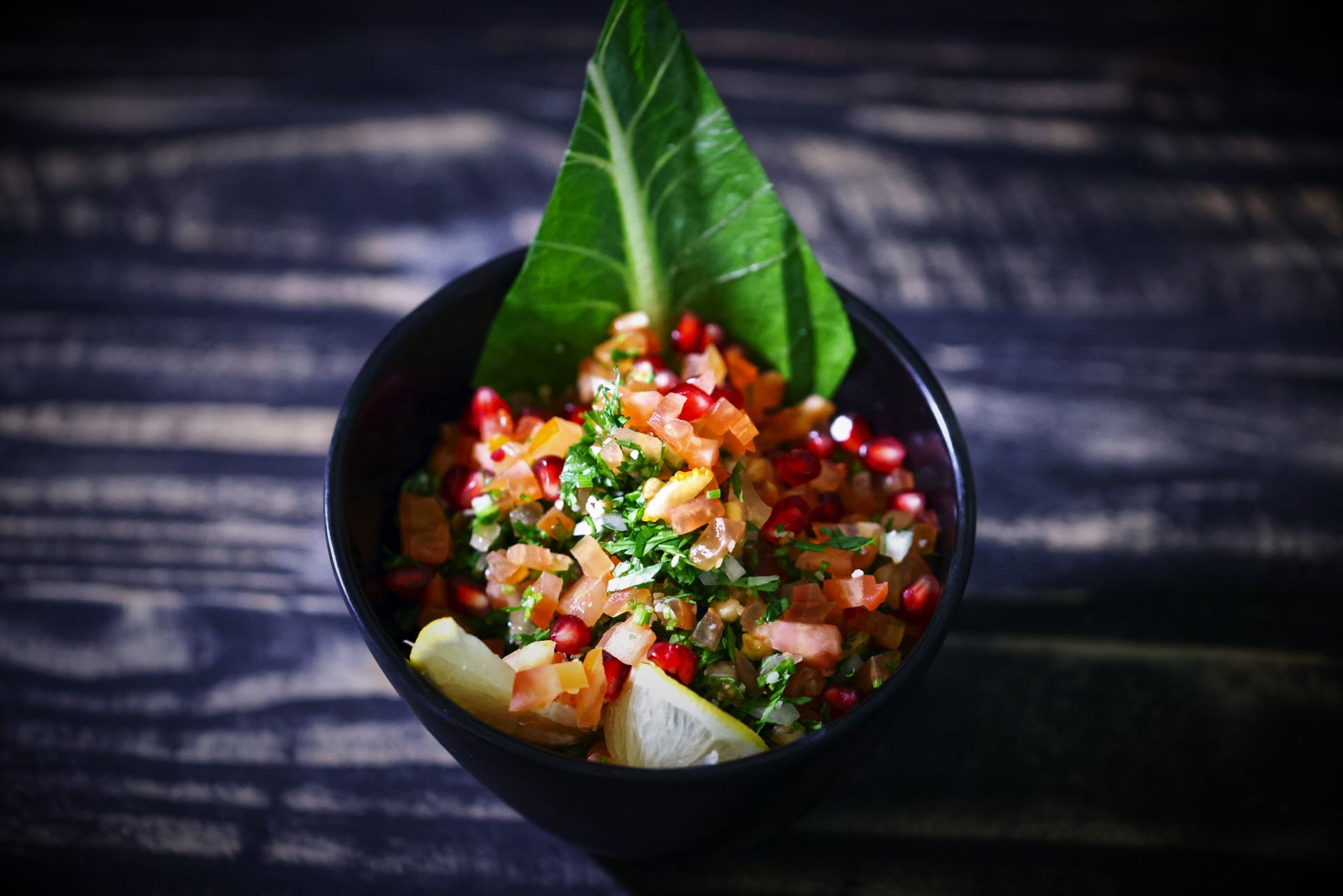Bright and colorful fresh salsa in a black bowl with a rustic background, featuring pomegranate, tomato, and herbs.