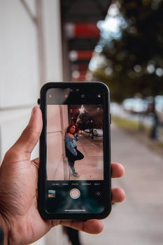 A person holds a smartphone capturing an outdoor portrait on a city street.