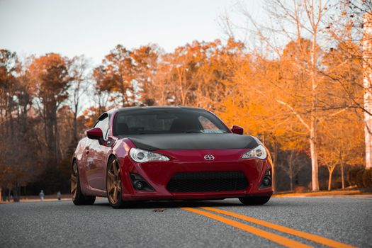 A vibrant red sports car parked on a scenic autumn road with golden foliage.