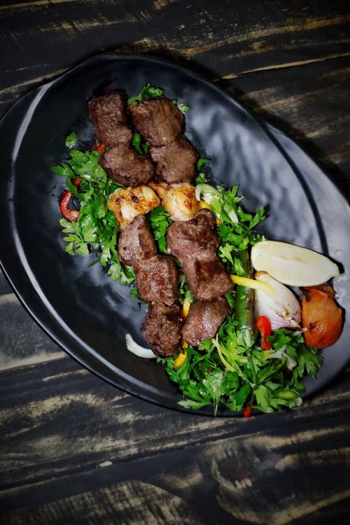 Free Mouthwatering grilled kebab served with fresh greens and grilled vegetables on a dark plate. Stock Photo