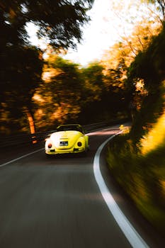 A classic yellow Volkswagen Beetle speeds through a winding forest road, capturing motion and adventure.