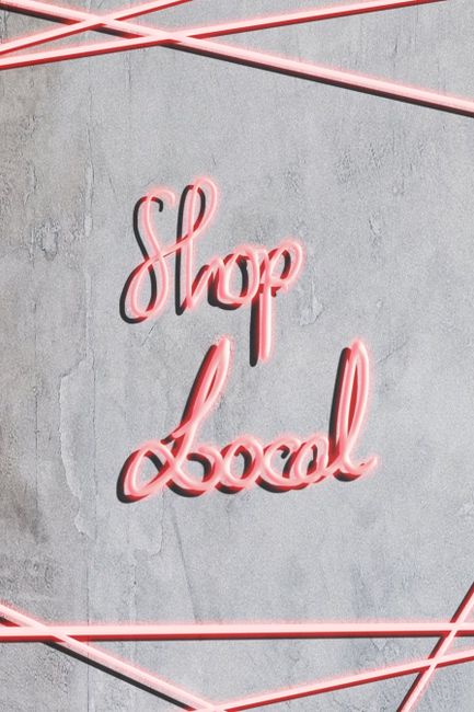 Bright neon 'Shop Local' sign on concrete wall background, promoting local shopping.