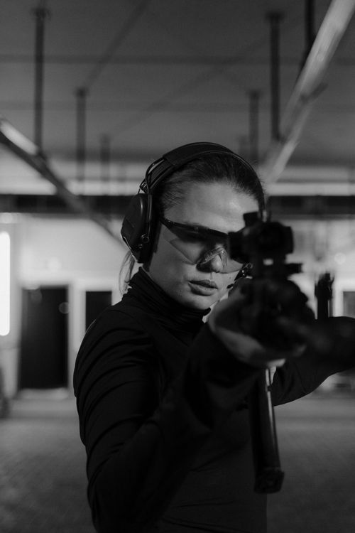 Woman holding a rifle at an indoor shooting range, grayscale photo
