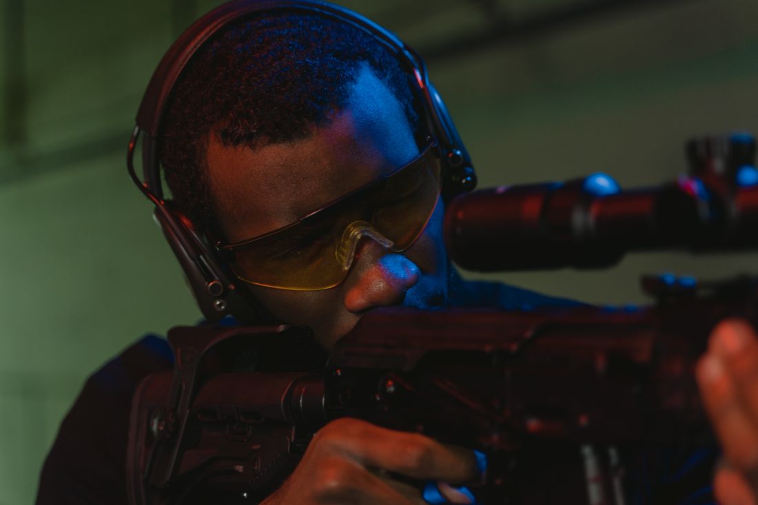 Shooter aiming a rifle while wearing safety glasses and earmuffs at an indoor range, illustrative stock photo
