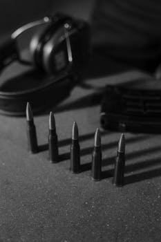 Monochrome image of bullets, headphones, and magazine on a concrete surface.