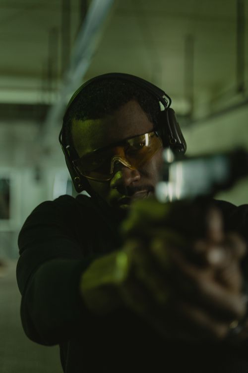 Free Man wearing eye and hearing protection aiming a handgun at an indoor shooting range. Stock Photo