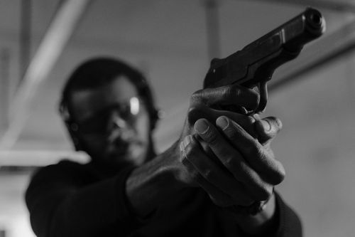 Free Black and white photo of a man aiming a handgun at an indoor shooting range. Stock Photo