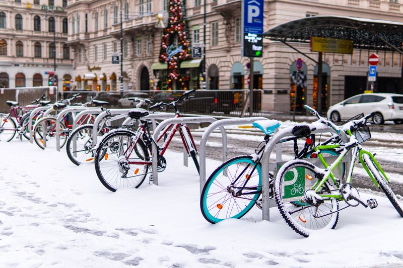 Snow-covered bicycles parked on a winter street in Vienna, Austria, with classic architecture in the background.