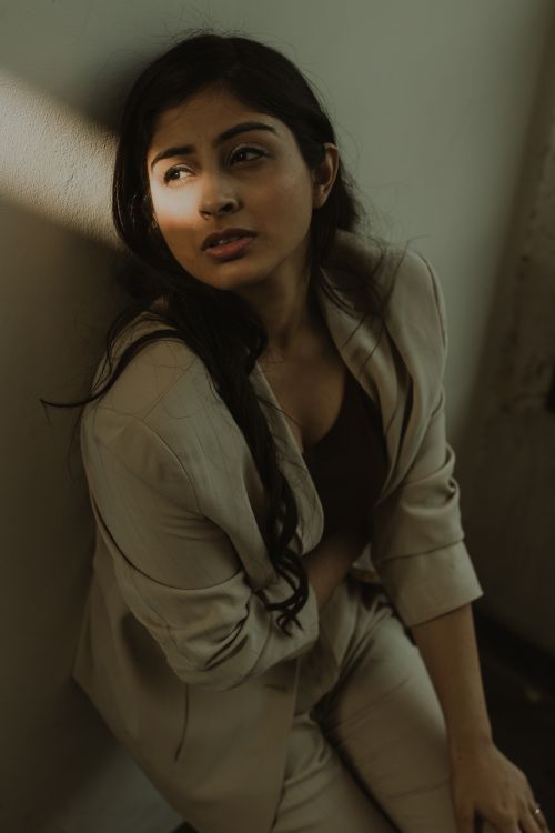Free From above of tired ethnic female with dark hair in casual clothes standing near wall illuminated by sunbeam and looking away Stock Photo