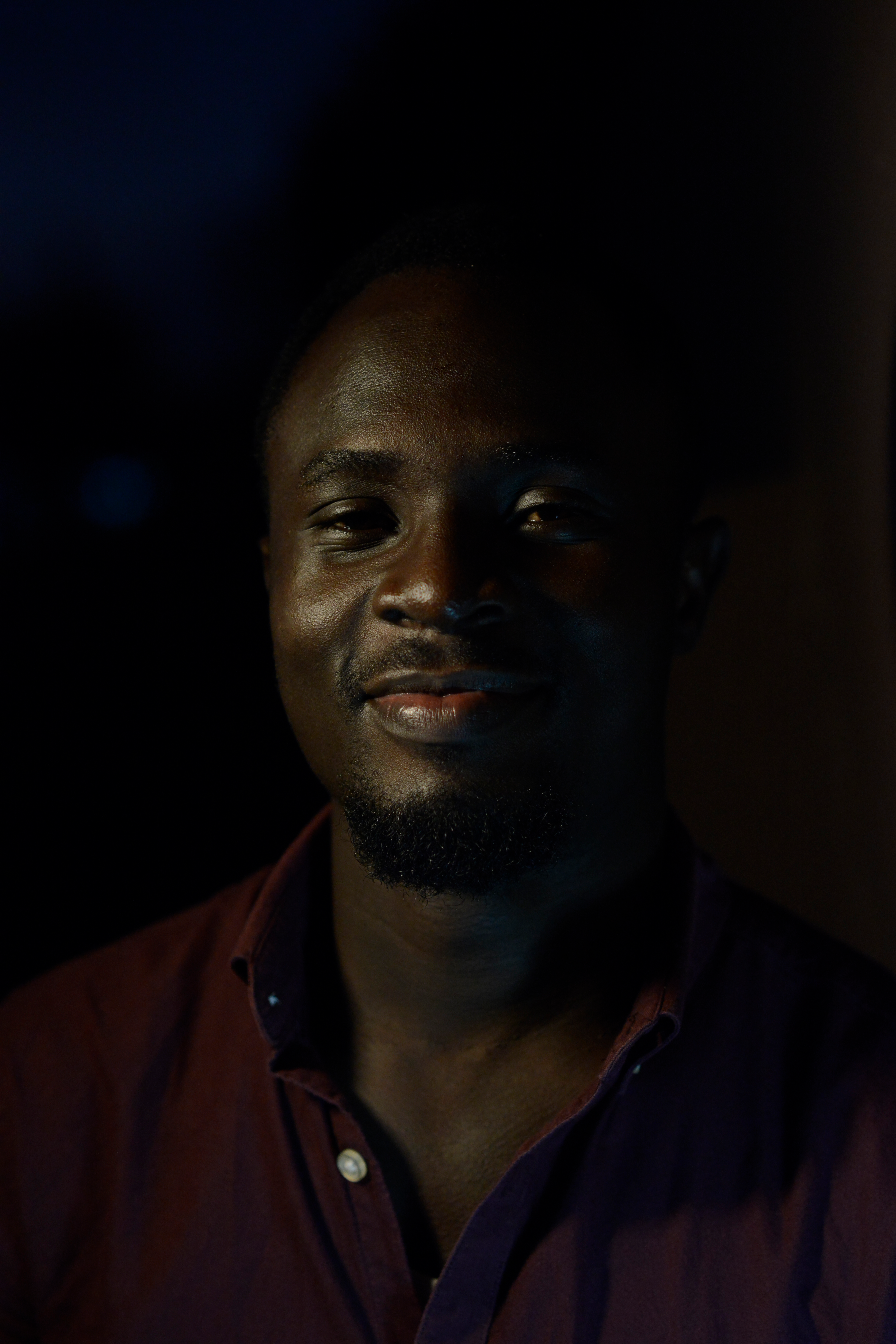 A smiling man poses in a shadowy setting, creating a moody portrait effect.