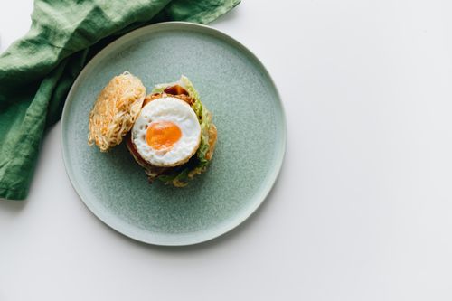 Free Delicious ramen burger topped with a sunny-side egg on a ceramic plate, perfect for food enthusiasts. Stock Photo